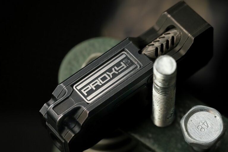 Close-up of a black PROXY device on a metal surface, featuring intricate design details and adjacent metal fasteners, highlighting its industrial aesthetic and functionality.