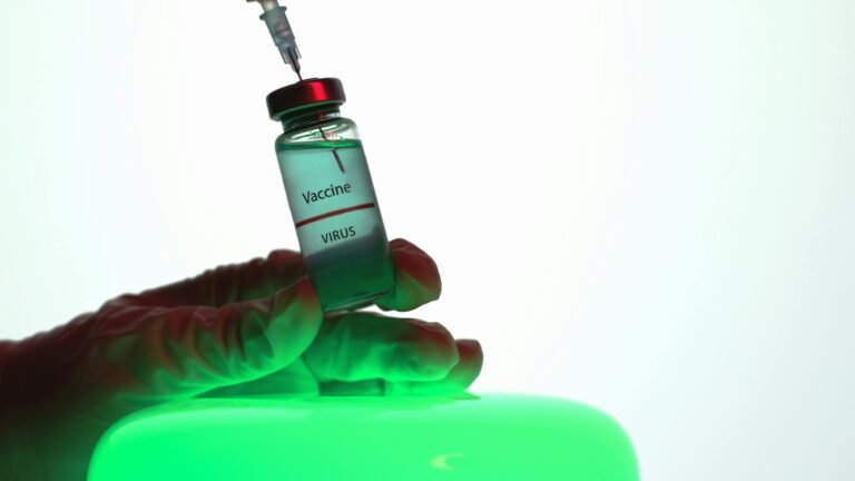 Close-up of a hand holding a vaccine vial labeled "Vaccine" and "Virus," with a syringe poised above it, set against a softly lit green background, symbolizing medical advancements and immunization efforts.