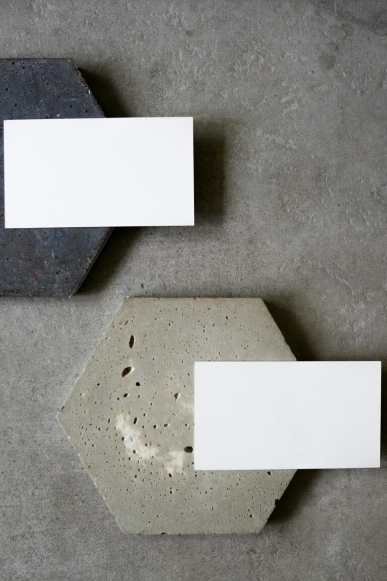 Two hexagonal concrete slabs in gray and light beige serve as a backdrop for blank white business cards, showcasing a minimalist design aesthetic. The image highlights the texture and color contrast between the concrete and the cards, ideal for branding or design inspiration.